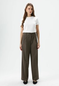 White short-sleeve t-shirt paired with high-waisted, wide-leg olive green trousers, featuring a front button closure. Black flat shoes.