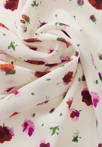 Tessuto leggero e cremoso con una superficie liscia, caratterizzato da un motivo floreale in tonalità di rosso, rosa e verde su una superficie spiegazzata.