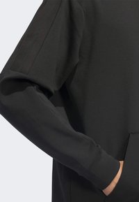 Black sweatshirt with a smooth texture, featuring a kangaroo pocket and three vertical stripes on the sleeve. Simple, modern design.