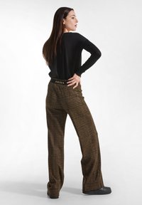 Black long-sleeve top paired with brown checkered high-waisted wide-leg trousers. The trousers feature a branded elastic waistband.