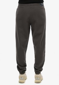 Pantalones de chándal gris oscuro con puños elásticos y bolsillos laterales, fabricados en tela suave. Presenta un parche de logo en la cintura.