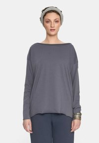 Szary, długi rękaw, top z dekoltem w łódkę, luźny krój i lekki materiał. Połączony z ciemnymi spodniami i fakturowaną opaską na głowę.