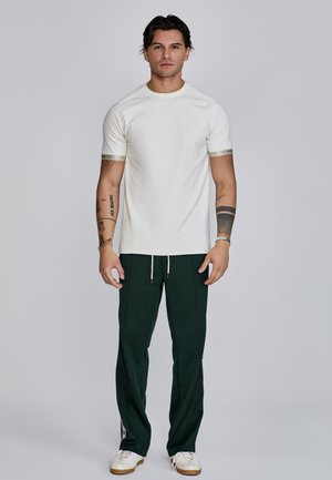 Short-sleeve, cream t-shirt with a round neck and contrasting light green cuffs, paired with dark green pants and white sneakers.
