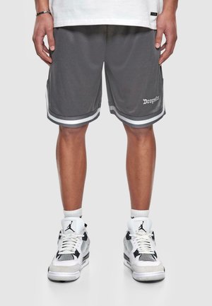 Personne portant un short de basket gris avec des bandes blanches et un texte sur la jambe, associé à des baskets montantes blanches avec des détails noirs.