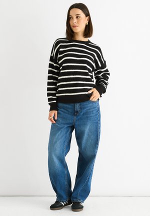 Black and white striped sweater in a chunky knit design, paired with high-waisted blue jeans and black sneakers.