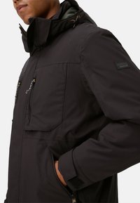 Schwarz wasserfeste Jacke verfügt über eine Kapuze, zwei Fronttaschen mit Reißverschlüssen und verstellbare Bündchen. Hergestellt aus einem glatten, strapazierfähigen Material.