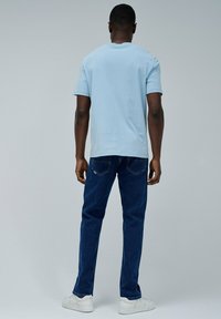 Camiseta de manga corta azul claro combinada con jeans azul oscuro y zapatillas blancas. Detalles de costura visibles en los jeans y textura de tela suave.