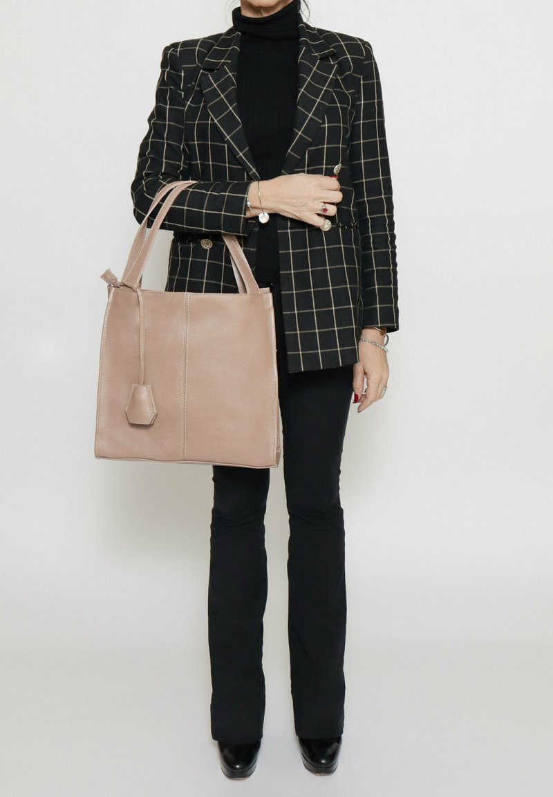 Beige leren totebag met gestructureerde vorm, dubbele handvaten en een decoratieve tassel. Draag met een zwart-wit geblokte blazer en zwarte broek.