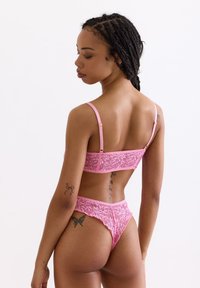 Roze kanten lingerieset met een bralette met verstelbare bandjes en bijpassende hoge taille slip, waarbij ingewikkelde bloemenpatronen worden getoond.