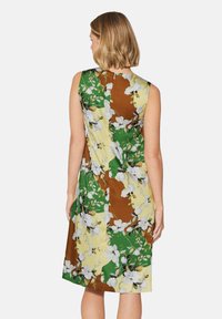 Blumenkleid mit einem ärmellosen Design. Enthält ein Patchwork aus Gelb, Grün und Braun mit weißen Blumenmustern. Weicher Stofftextur.