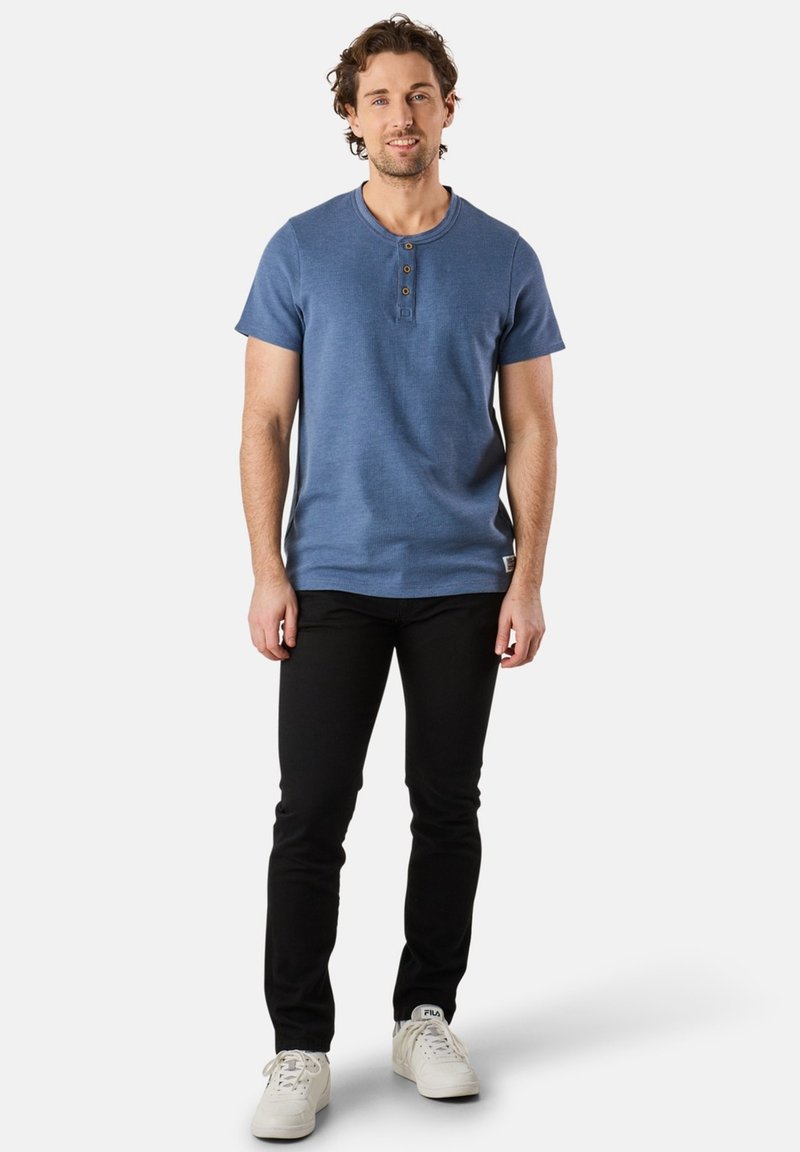 Blue short-sleeve henley shirt with three button placket, paired with black slim-fit jeans and white sneakers. Casual, everyday wear.