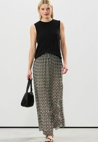 Top senza maniche nero abbinato a una lunga gonna a fantasia con forme geometriche in tonalità crema e nera. Modella che tiene una borsa nera.