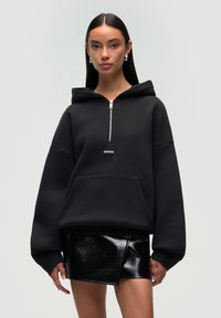 Czarna bluza z kapturem na zamek błyskawiczny z dużą kieszenią z przodu, w oversize'owym fasonie, wykonana z gładkiego, teksturowanego materiału. Z przodu znajduje się małe logo.