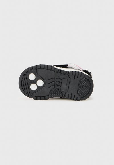 Black rubber shoe sole with tread patterns and three circular indentations, featuring a textured grip and flat edges for stability.