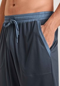 Shorts de sport pour homme en tissu gris foncé, dotés d'une taille avec cordon de serrage et de poches latérales avec des accents bleus contrastants. Texture lisse.