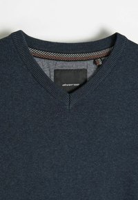 Ciemnoniebieski sweter z dekoltem w serek, z prążkowanym wykończeniem i paskowanym materiałem wewnątrz dekoltu, na którym znajduje się czarna etykieta marki.