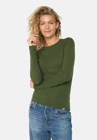 Langærmet grøn skjorte i et blødt, tekstureret stof med en rund halsudskæring, parret med lyseblå jeans. Brandmærke synligt i bunden.