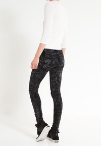 Černé úzké džíny s texturou a vybledlým vzorem, v kombinaci s bílým žebrovaným tričkem s tříčtvrtečními rukávy a černými kotníkovými teniskami.