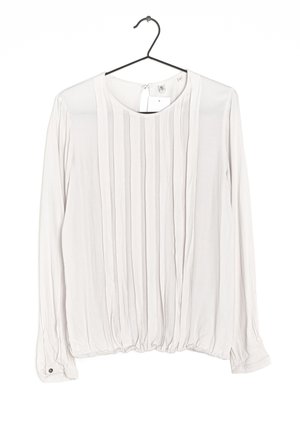 Bílá halenka s dlouhým rukávem s vertikálními sklady, kulatým výstřihem, manžetami na knoflíky a elastickým lemem, zavěšená na černém ramínku.