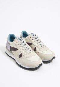 Zapatillas en gamuza beige y malla, con acentos en marrón oscuro, interior azul y una suela blanca texturizada con fondo negro.