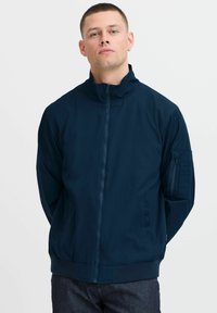 Jūrų laivyno zip-up jaketa su auk�štu apykakle, glotniais rankogaliais ir apatine dalimi, turinti naudingą kišenę ant rankovės ir lygų, matinį paviršių.