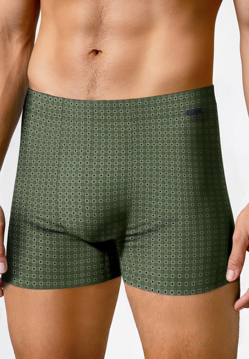 Mannelijke romp in groene boxershorts met een klein vierkant patroon, staand tegen een eenvoudige witte achtergrond.