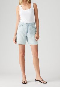 Lichtblauwe denimshorts met hoge taille en een ontspannen pasvorm, voorzien van twee zakken aan de voorkant en een knoopsluiting. Gecombineerd met een wit tanktopje.