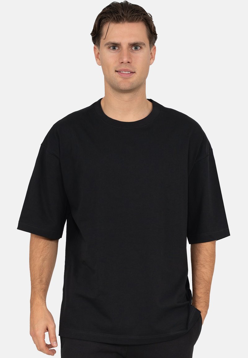 Zwart oversized katoenen T-shirt met korte mouwen en een ronde halslijn. Gladde textuur, minimale naden en geen zichtbare patronen of logo's.