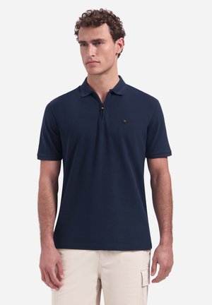 Mann trägt ein marineblaues kurzärmeliges Poloshirt mit Reißverschlusskragen und beige Cargohosen, steht vor einem schlichten Hintergrund.