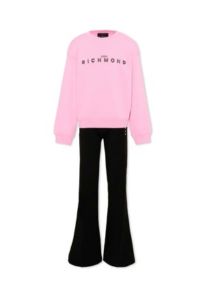 Felpa rosa a maniche lunghe con la scritta "John Richmond" abbinata a pantaloni neri a vita alta e a zampa su sfondo bianco.