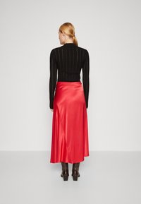 Svart stripete langermet topp med vertikale striper, kombinert med en gulvlang satinrød skjørt. Skjørtet har en glatt tekstur og faller elegant.