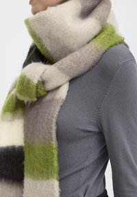 Écharpe en laine au toucher doux, avec un motif de bandes vertes, grises et crème, enroulée autour du cou.