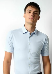 Hellblaues Poloshirt mit kurzen Ärmeln aus glattem Material, mit einer Knopfleiste und einem weichen Kragen mit strukturierten Akzenten.
