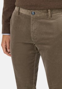 Pantaloni in corduroy marrone con sottili strisce verticali, un bottone di metallo blu e design frontale piatto, dal texture liscia.