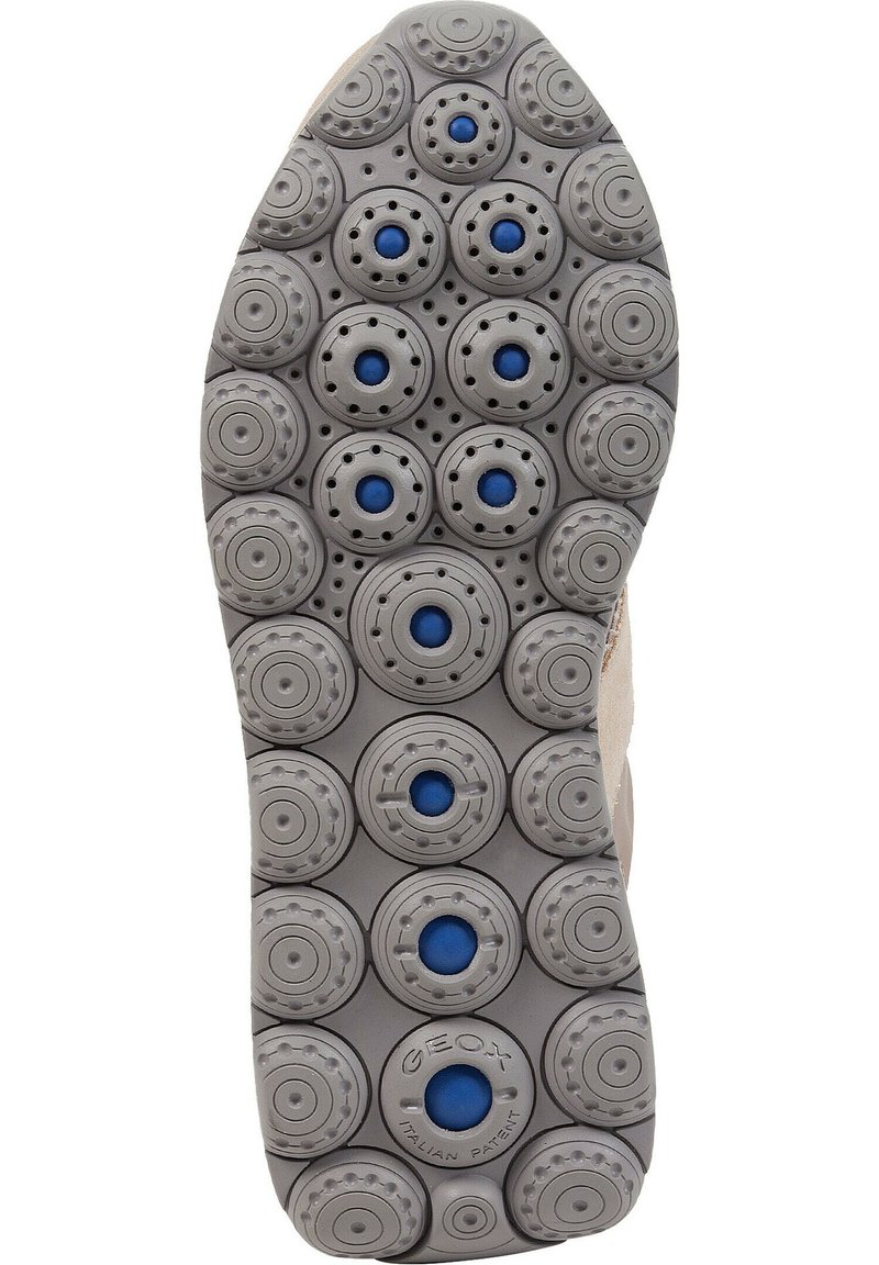 Semelle de chaussure en caoutchouc gris avec des motifs circulaires, accents bleus dans les trous et surfaces texturées pour une meilleure adhérence.