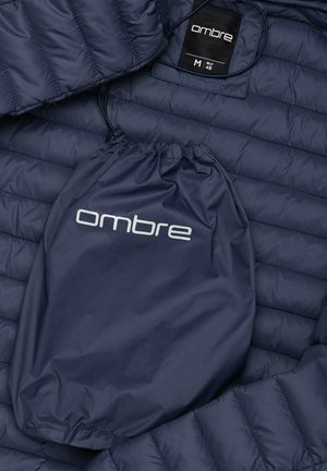 Marineblaue Steppjacke mit einem gesteppten Design, aus leichtem Material. Enthält einen Zugbeutel mit dem "Ombre"-Logo. Größe M.
