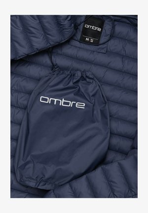 Marineblaue Steppjacke mit einem gesteppten Design, aus leichtem Material. Enthält einen Zugbeutel mit dem "Ombre"-Logo. Größe M.