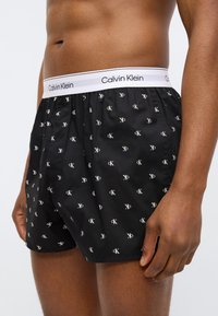 Μαύρα μποξέρ με λευκό μοτίβο λογότυπου CK, ελαστική μέση Calvin Klein, άνετη εφαρμογή, απαλό ύφασμα και τελειώματα με ρέλι.