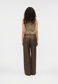 Καφέ παντελόνι με φαρδιά μπατζάκια και λεία υφή, με θηλιές για ζώνη, συνδυασμένο με εφαρμοστό τοπ σε ελιά πράσινο χρώμα, από πίσω.