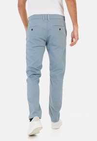 Lichtblauwe chino's van katoen, met twee achterzakken met donkere knopen, slim fit, en gecombineerd met witte sneakers.