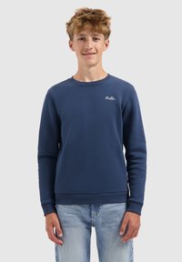 Marineblauwe sweatshirt van zachte stof, met ribgebreide manchetten en onderrand, en een geborduurd logo op de borst. Gecombineerd met lichte jeans.