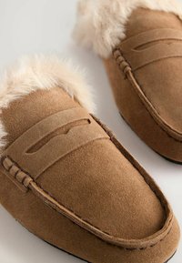 Pantoufles en suède marron avec un doux revers en fausse fourrure, dotées d'un motif décoratif brodé et d'une silhouette de style mocassin.
