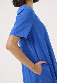 Sininen rento mekko, valmistettu pehmeästä kankaasta, jossa on lyhyet hihat, pyöreä pääntie ja sivutaskut. Meko on väljää mallia ja yksinkertaisella designilla.