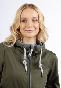 Giacca leggera verde oliva con cappuccio grigio, dotata di minuteria argentata, lacci intrecciati e chiusura a zip completa.