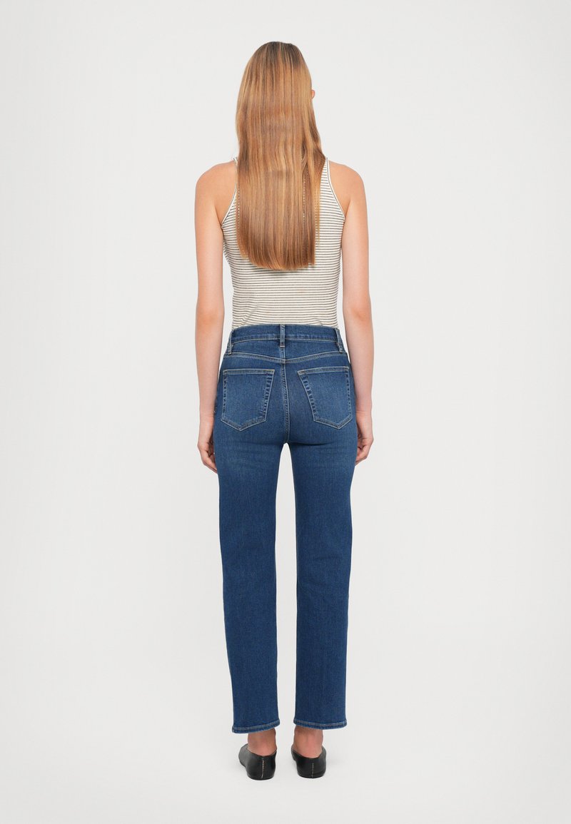 Hogwaisted blauwe jeans van stevig denim, met een rechte pijp, vijf zakken en een zichtbare rits. Draagt met een gestreepte tanktop.