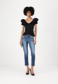 Top nero senza spalline con maniche a volant; abbinato a jeans skinny blu chiaro; modella che tiene una pochette grigia strutturata; tacchi alti neri.