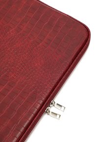 Czerwony skórzany pokrowiec na laptopa o teksturze krokodyla, z zamknięciem na srebrny zamek błyskawiczny i podwójnymi metalowymi uchwytami zamka.