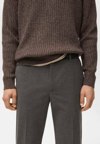 Suéter marrón de punto acanalado con acabado texturizado, combinado con pantalones grises de corte sastre con una tela suave. Detalle visible en la pretina.