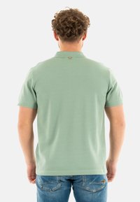 Camisa de polo verde menta de manga corta, con cuello acanalado y un detalle de botón en la parte posterior, combinada con pantalones vaqueros azules.
