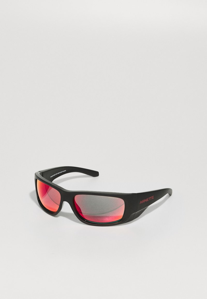 Lunettes de soleil noires au design élégant, verres gris avec un dégradé rouge et un discret branding "ARNETTE" sur les branches.